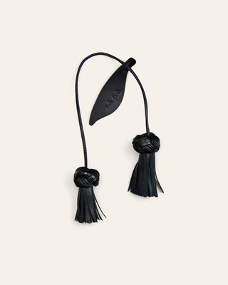 Cala Jade leather bag charm in black shaped as a flower on a beige background