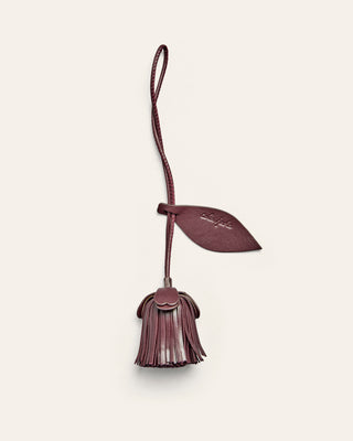 A flower shaped leather bag charm in burgundy on a beige background