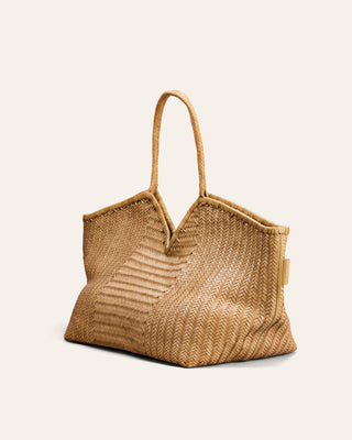 A large natural woven leather tote bag with a single top handle, displayed against a solid off-white background.