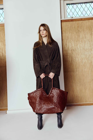 Cala Jade Humi XL - Woman holding a brown textured bag indoors with wooden paneling.