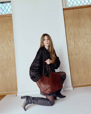 Cala Jade humi - Woman holding a brown leather bag against a white wall with wooden panels.