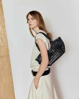 Woman wearing a black woven bag on a plain background
