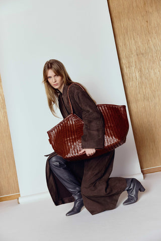 Woman holding a large brown textured bag against a white wall.