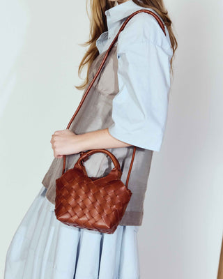 Woman holding a brown handbag against a plain background