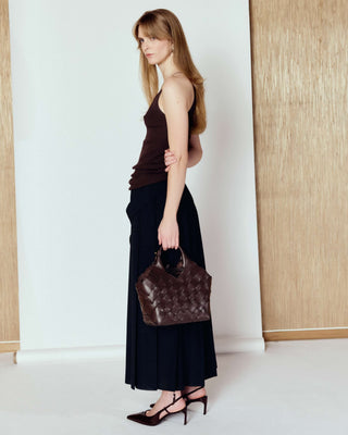Woman holding a brown handbag in a minimalistic setting with white walls and wooden panels.