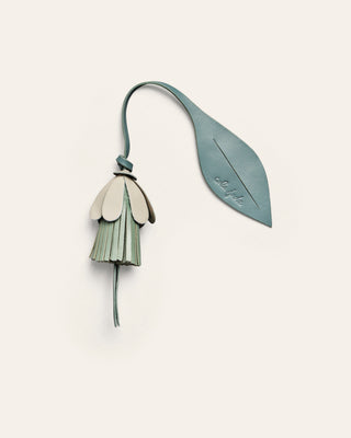 A green, white and blue leather bag charm on a beige backgrounf