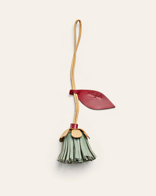 A flower shaped leather bag charm in red, yellow and blue on an beige background