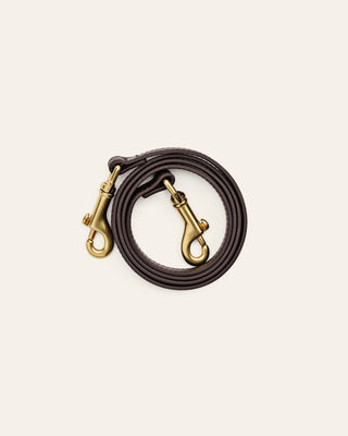 A brown shoulder strap with brass hardware on a beige backgrounf