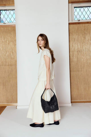 Woman in a white dress holding a black handbag against a minimalistic background