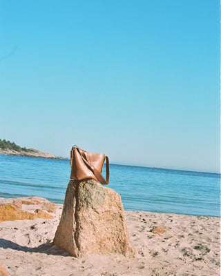A brown leather bag standing on a rock in front of the ocean