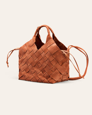 A woven leather handbag in a warm cognac brown, featuring dual top handles and a long shoulder strap, set against a solid off-white background.