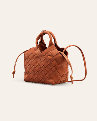 A small woven leather handbag in a warm cognac brown, featuring a structured basketweave pattern, a top handle, and thin drawstring ties on the sides, set against a solid off-white background.