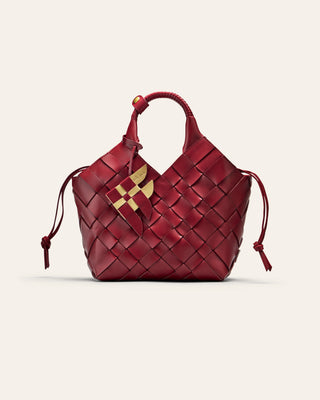 A red woven leather bag with a fish shaped bag charm on a beige background