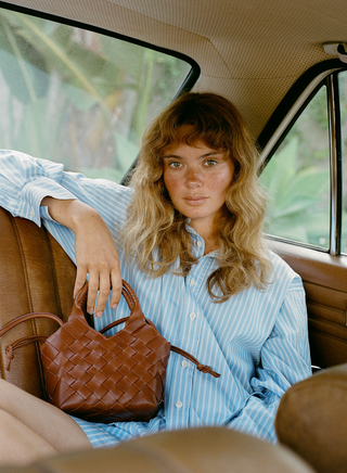 Woman sitting in a car holding a brown woven handbag