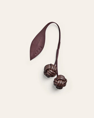A cherry shaped leather bag charm on a beige background