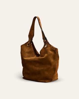 A slouchy brown suede hobo bag with dual shoulder straps and metal grommets, photographed on a clean off-white background.