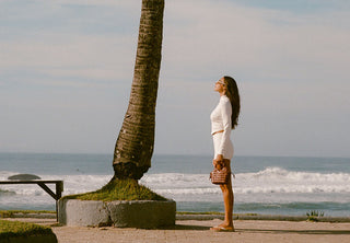 Woman standing on a beach path with a palm tree and ocean view