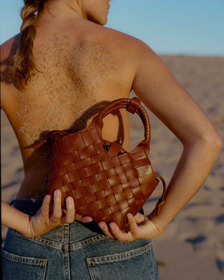 a woman holding i brown woven leather bag seen from the back
